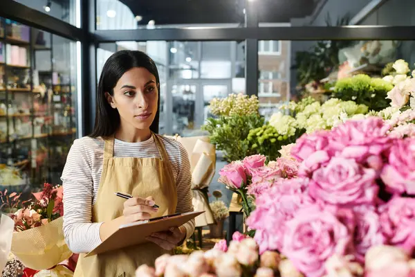 Una mujer morena arregla cuidadosamente hermosas flores mientras maneja sus tareas de floristería. - foto de stock