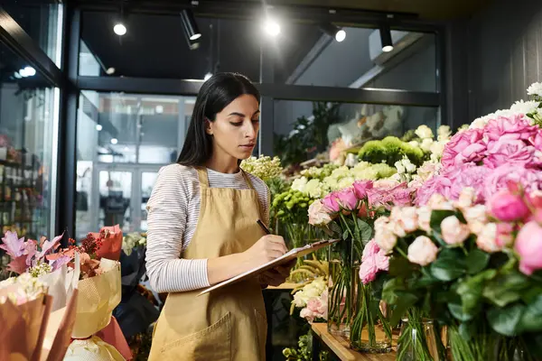 Una florista experta atiende a su tienda de flores, arreglando cuidadosamente ramos y anotando notas. - foto de stock