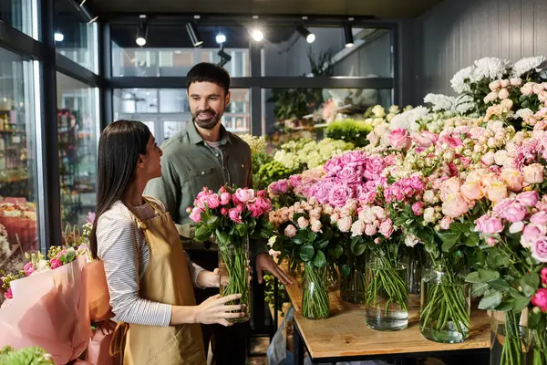 Una florista dedicada está ayudando a un cliente masculino a elegir hermosas flores en su encantadora tienda.. - foto de stock