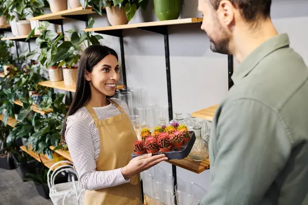 Hermosa floristería se involucra con un cliente masculino mientras muestra plantas coloridas en la tienda. - foto de stock