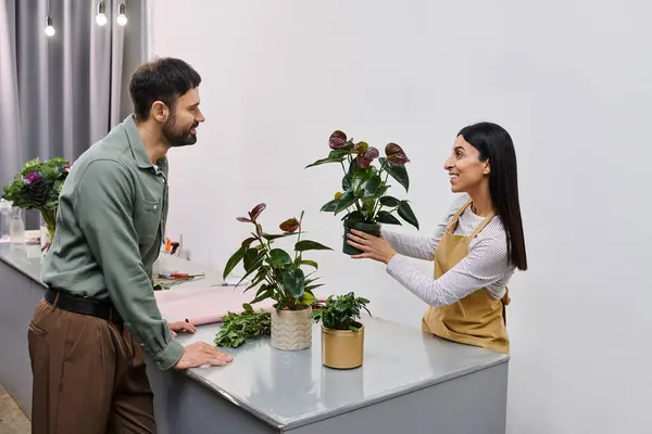 Fiorista si impegna con un cliente maschile, mettendo in mostra le piante in un ambiente affascinante negozio di fiori. — Foto stock