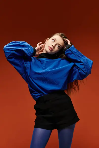 Une femme dynamique et élégante pose élégamment avec ses mains dans les cheveux sur un fond orange audacieux. — Photo de stock
