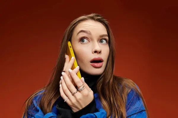 A vibrant stylish woman talking on a yellow phone with a surprised expression in a warm setting. — Stock Photo