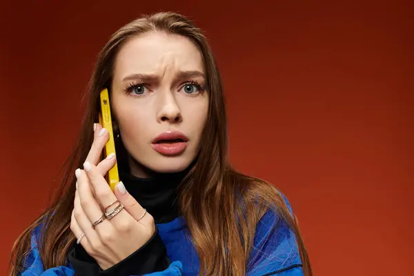 Mulher bonita com cabelo longo e ondulado expressa surpresa ao segurar um telefone amarelo. — Fotografia de Stock