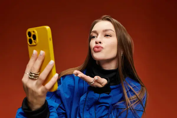 Donna vibrante cattura un selfie mentre soffia un bacio di fronte a uno sfondo colorato. — Foto stock