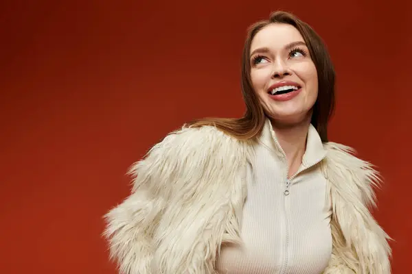 A stylish woman in a white fur coat smiles confidently against a warm backdrop. — Stock Photo