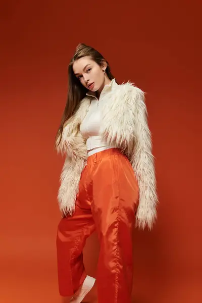 Uma mulher na moda posa confiantemente em uma roupa ousada contra um rico pano de fundo laranja. — Fotografia de Stock