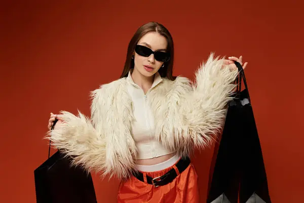 Una mujer con estilo sostiene bolsas de compras contra un telón de fondo vibrante, radiante alegría. - foto de stock