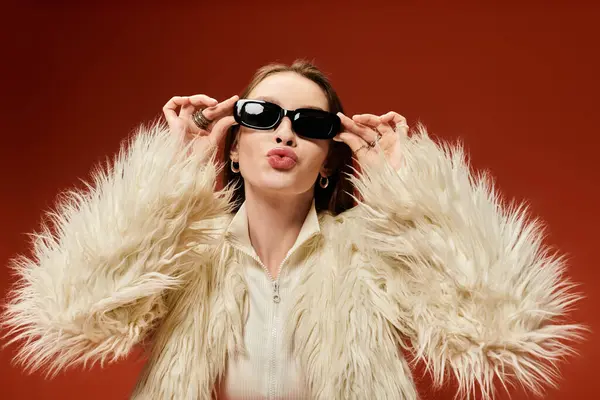A playful woman in stylish sunglasses poses before a vibrant red backdrop. — Stock Photo