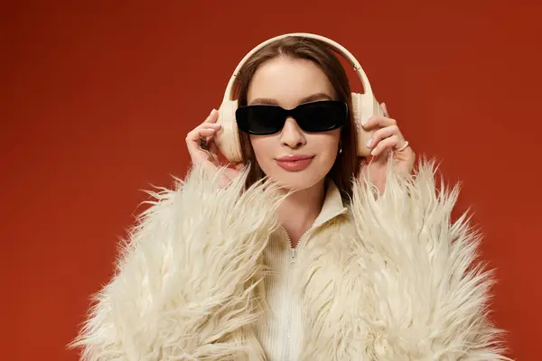 A stylish woman in a fur coat and sunglasses poses against a bright orange backdrop. — Stock Photo