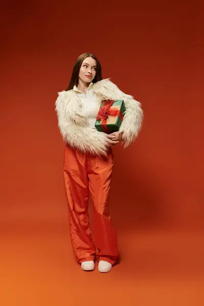 Confident woman holds a colorful gift against a bright orange background. — Stock Photo