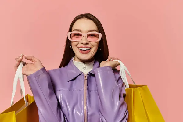 Una mujer elegante con una sonrisa alegre disfruta de una juerga de compras, sosteniendo bolsas de color amarillo brillante. - foto de stock
