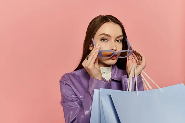 Una mujer con estilo posa con bolsas de compras y gafas de sol en un entorno vibrante y alegre. - foto de stock