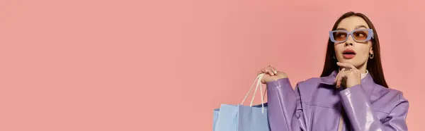 Vibrant woman in stylish outfit poses with shopping bags against a pink backdrop. — Stock Photo