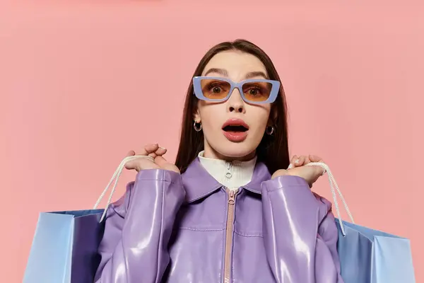 Mujer con una elegante chaqueta púrpura muestra sorpresa mientras sostiene bolsas de compras de una manera lúdica. - foto de stock