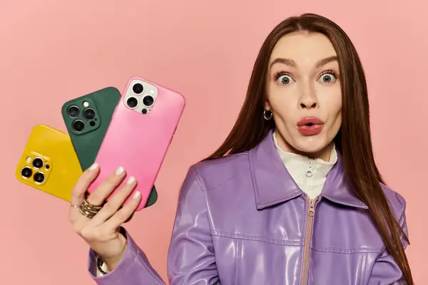 Стильная женщина держит четыре красочных смартфона, выражая волнение в игривой позе. — стоковое фото