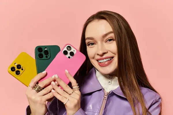 A vibrant stylish woman smiles while holding colorful mobile phones in her hands. — Stock Photo