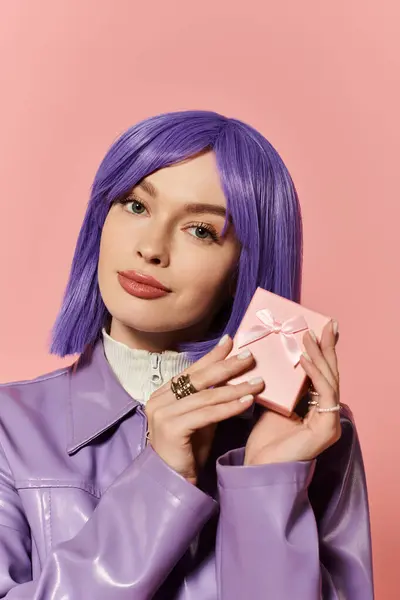Woman with a vibrant purple hairstyle presents a pink gift box in front of a soft pink backdrop. — Stock Photo