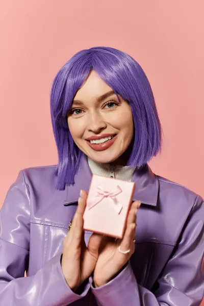 A vibrant stylish woman proudly displays a pink gift box, smiling with joy in a playful setting. — Stock Photo