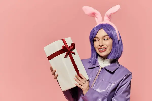 A woman with purple hair and bunny ears happily presents a wrapped gift in vibrant colors. — Stock Photo