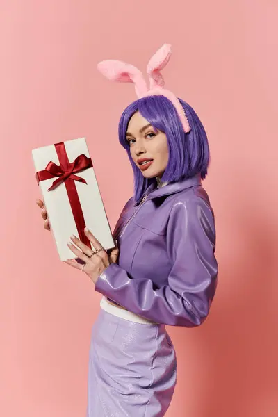 Stylish woman with purple hair smiles holding a wrapped gift against a pink backdrop. — Stock Photo