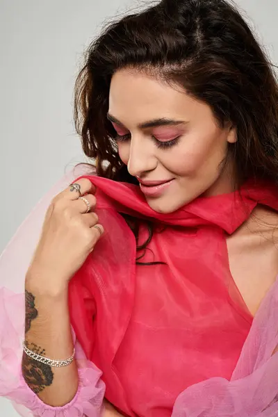 Young woman smiling while holding her pink scarf against her shoulders in a bright setting — Stock Photo