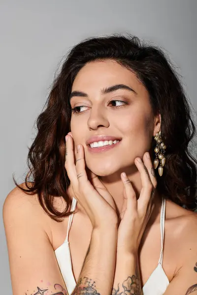 Beautiful young woman displays a joyful expression while touching her face in a studio backdrop — Stock Photo