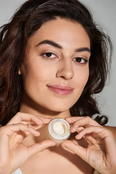 Beautiful young woman holds a skincare product with a radiant expression in natural light. — Stock Photo