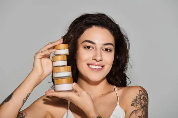 A young woman with dark hair proudly holds skincare jars, radiating confidence and beauty. — Stock Photo