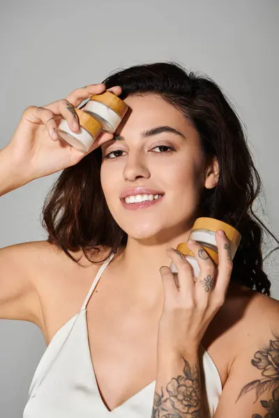 Woman smiles while holding jars of skincare cream, highlighting beauty and self care. — Stock Photo