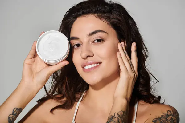 Beautiful young woman holds a jar of skincare cream while posing with a smile in studio lighting — Stock Photo