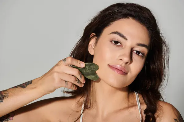 Beautiful young woman enjoying a rejuvenating facial massage with a jade roller indoors. — Stock Photo