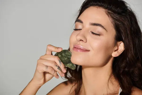 Woman relaxes while using a jade roller on her face in a bright indoor setting. — Stock Photo