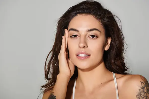 Jovem mulher acaricia suavemente sua bochecha, mostrando sua beleza radiante em iluminação suave. — Fotografia de Stock