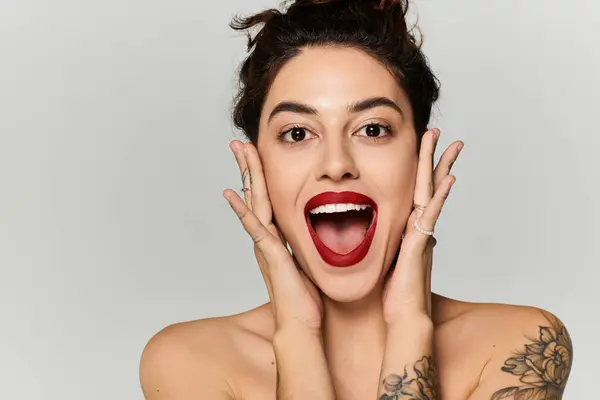 A young woman beams with joy, her hands on her face accentuating her red lips. — Stock Photo