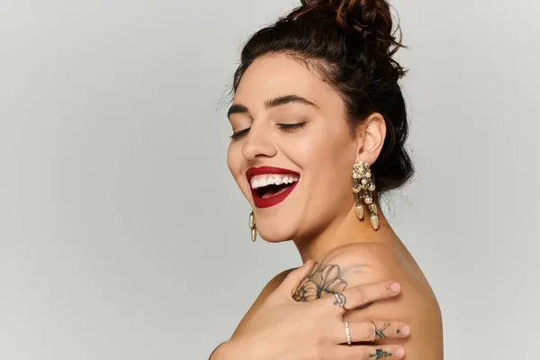 Smiling young woman with a joyful expression displays her elegant earrings and tattoos. — Stock Photo