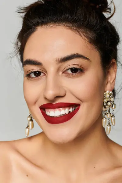 Young woman radiates beauty with striking earrings and vibrant lipstick in a studio. — Stock Photo