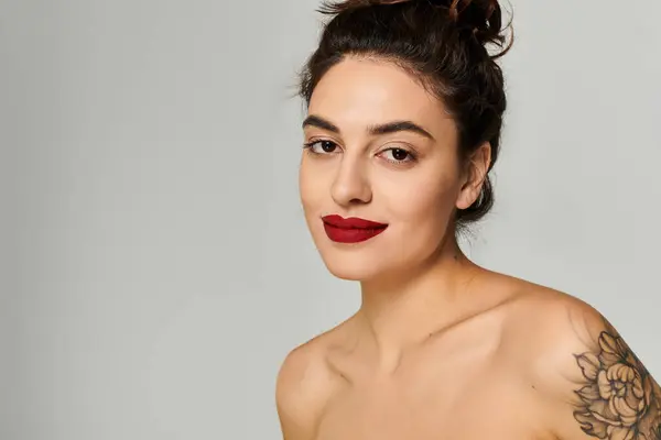 Beautiful woman showcases her striking red lips and floral tattoo in a minimal setting. — Stock Photo