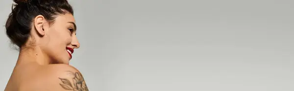 Una giovane donna sorride con grazia, mostrando il suo splendido tatuaggio in un ambiente interno calmo. — Foto stock