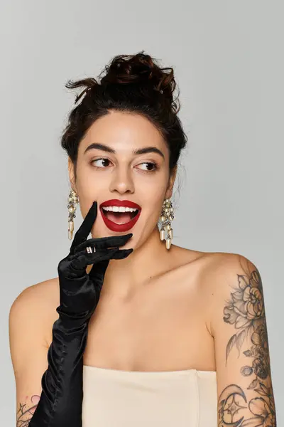 Young woman with striking tattoos smiles playfully while wearing elegant earrings and gloves. — Stock Photo