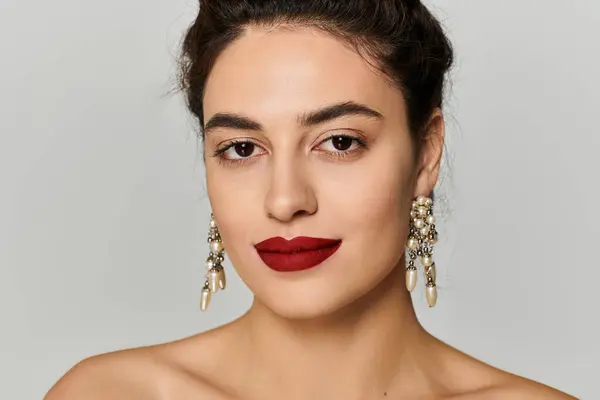 Mujer joven muestra maquillaje elegante y pendientes distintivos en un entorno elegante. - foto de stock