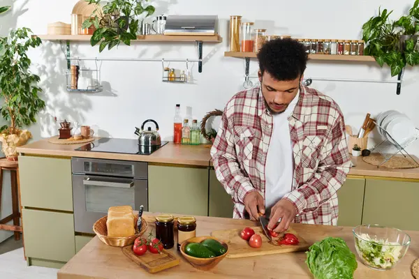 Attractive young man skillfully chops tomatoes amid fresh veggies in a bright kitchen. — Stock Photo