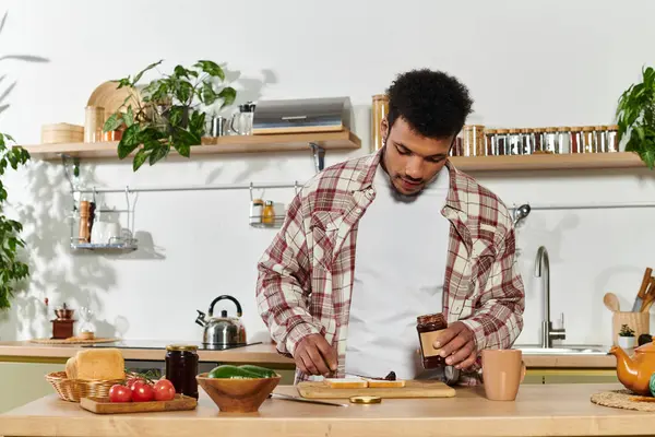 Man spreads jam on bread while enjoying a quiet morning in a bright kitchen. — Stock Photo