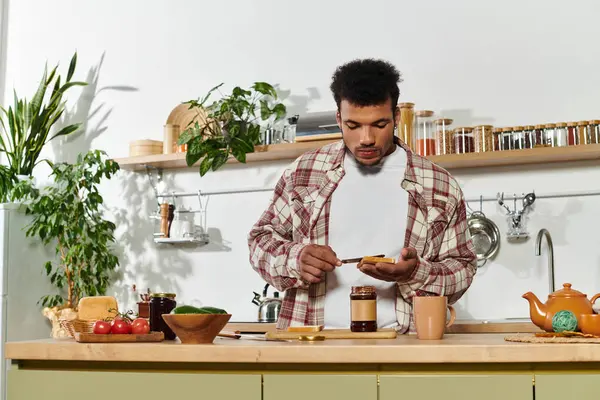 Schöner junger Mann verteilt Marmelade auf Toast, während er einen entspannten Moment in seiner Küche genießt. — Stockfoto