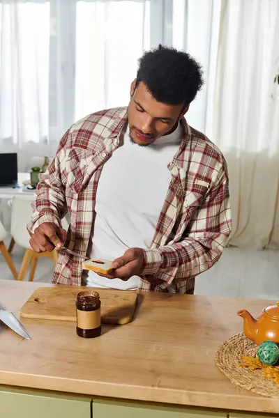 A young handsome man spreads jam on toast while enjoying a sunny morning at home. — Stock Photo