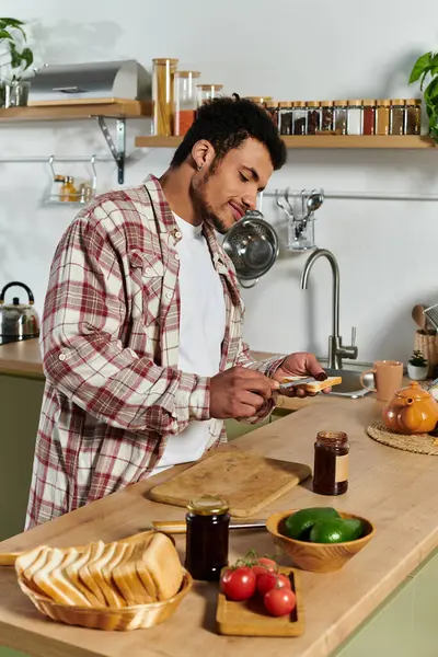 Handsome young man spreads jam on sliced bread while enjoying his time in the kitchen. — Stock Photo