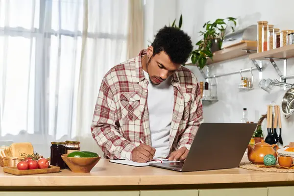 Man focuses on a notebook while cooking in a bright and stylish kitchen space. — Stock Photo