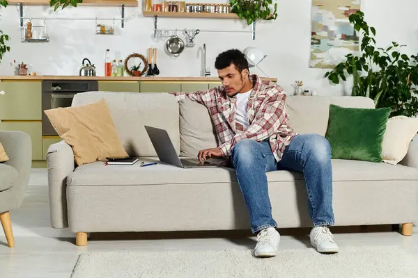 A young man is focused on his laptop, sitting comfortably in a stylish living room with plants. — Stock Photo