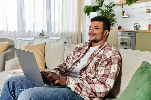 Young man smiles while typing on a laptop in a bright and inviting living room. — Stock Photo