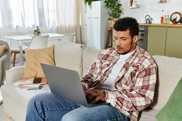 A young handsome man sits comfortably on a sofa, focused on his laptop in a stylish living area. — Stock Photo